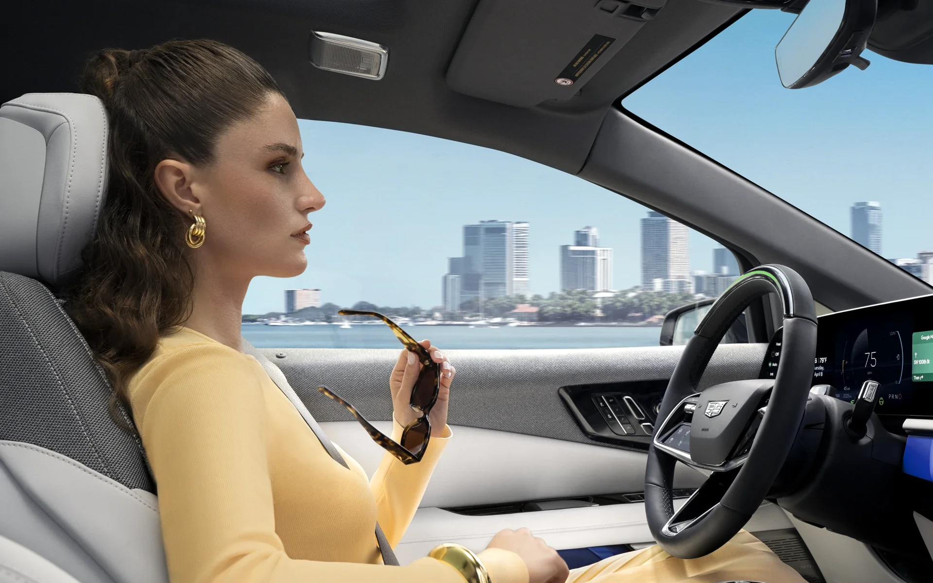 Passenger View of a Woman Driving a Cadillac OPTIQ Past the City While Utilizing Super Cruise Hands-free Technology
